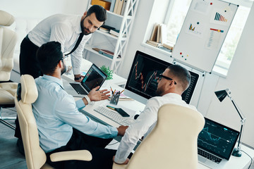 Sharing opinions. Group of young modern men in formalwear analyzing stock market data while working in the office