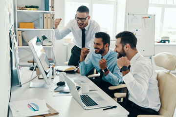 Fototapeta premium Finally success. Group of young modern men in formalwear smiling and gesturing while working in the office