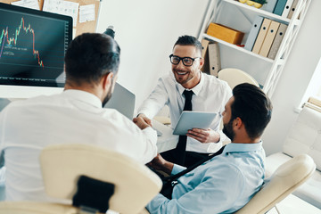 Obraz premium Congratulations! Young men in formalwear shaking hands while working in the office