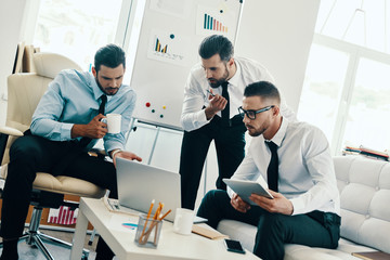 Successful business team. Group of young modern men in formalwear working using technologies while sitting in the office