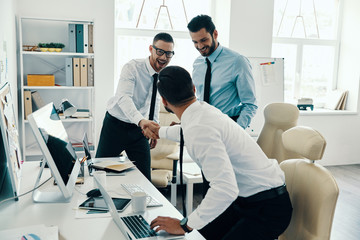 Obraz premium Welcome on the board! Young modern men in formalwear shaking hands while working in the office