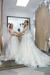 Two happy women in wedding dresses posing in salon