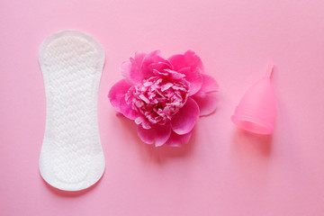 choice of women intimate hygiene products, sanitary pad, reusable silicone menstrual cup and beautiful fresh peony flower on pink background, flat layout, top view