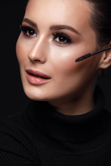 Beauty Cosmetics.Woman applying black mascara on eyelashes with makeup brush. photos of appealing brunette girl on black background.High Resolution