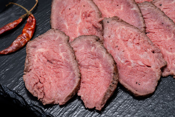 Sliced Grass Fed Juicy Corn Roast Beef garnished with dried Red Chile De Arbol Pepper on black natural stone background.