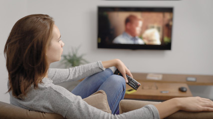 relaxed woman is watching films by tv screen in her home, sitting on a sofa in living room in holidays