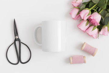 Top view of a mug mockup with a bouquet of pink roses and silk ribbons on a white table.