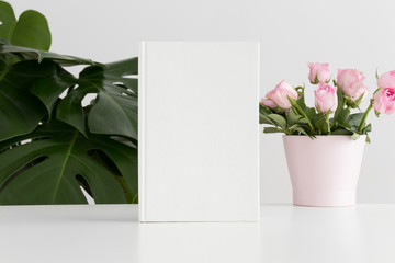 White book mockup with pink roses in a pot and a monstera plant.