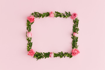 Floral wreath made of pink roses and green branches on a pink background.