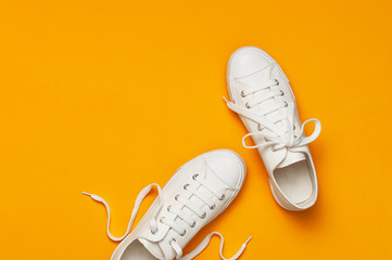 White female fashion sneakers on yellow orange background. Flat lay top view copy space. Women's shoes. Stylish white sneakers. Fashion blog or magazine concept. Minimalistic shoe background, sport