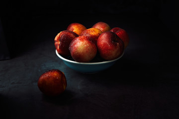 Fototapeta na wymiar Still life of fresh delicious sweet nectarines with droplets of water in a bowl on dark background. Low key.