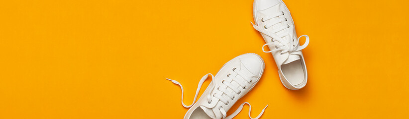 White female fashion sneakers on yellow orange background. Flat lay top view copy space. Women's shoes. Stylish white sneakers. Fashion blog or magazine concept. Minimalistic shoe background, sport - obrazy, fototapety, plakaty