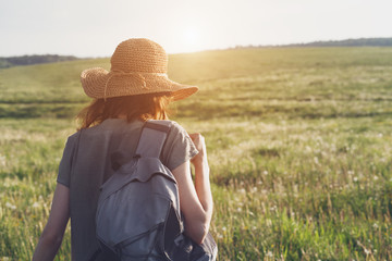 young woman wearing linen dress and straw hat with backpack enjoying nature an walking outside,...