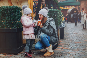 Mother with child girl drinking hot chocolate coffee at Christmas market celebrating New Year holiday. Family outdoor winter activity. Mom and daughter spend time together. Authentic lifestyle. - 274057039