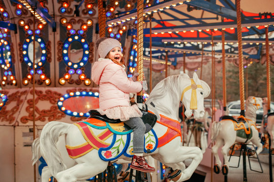 Adorable smiling Caucasian child girl riding on merry go round carousel horse at Christmas winter market outdoor. Happy child having fun celebrating New Year.