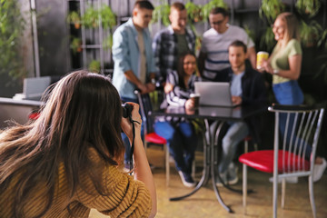 Woman taking photo of young coworkers during coffee break in cafe