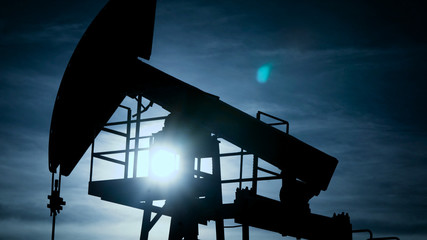 silhouette of large pampjack is pumping petroleum and gas out from beneath the earth surface...