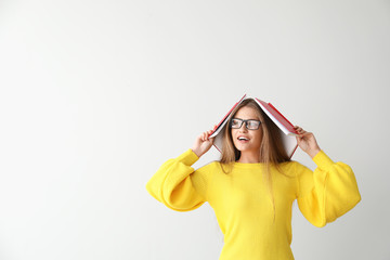 Funny young woman with books on light background