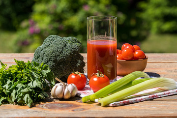 Fresh vegetables and tomato juice on old wooden table, over green nature background.