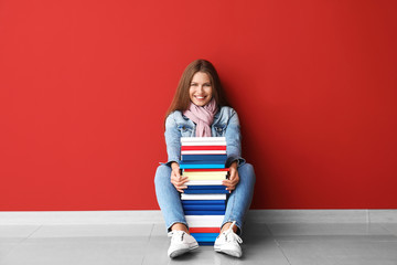 Beautiful young woman with books near color wall