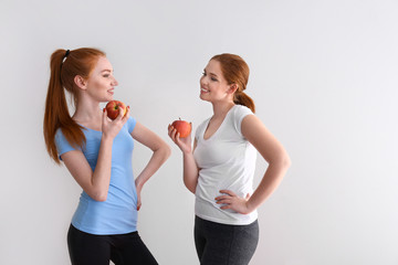 Beautiful young women eating fresh apples on light background