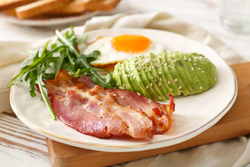 Plate with tasty fried egg, avocado and bacon on wooden table
