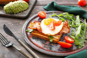 Plate with tasty grilled bread, fried egg and bacon on wooden table