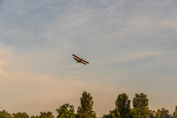 Small orange biplane airplane plane with propellers spraying crops with pesticides and herbicides against insects and plant diseases in the evening above the farm land