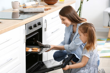 Young woman and her little daughter baking tasty cookies at home