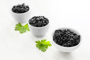 Fototapeta na wymiar Bowls with black caviar on light background