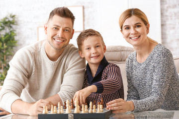 Happy couple with little adopted children playing chess at home