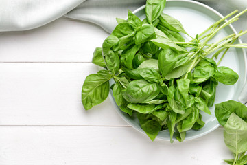 Plate with fresh basil on white wooden background