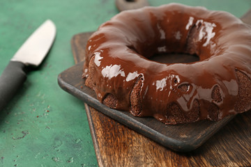 Wooden board with tasty chocolate cake on color background, closeup