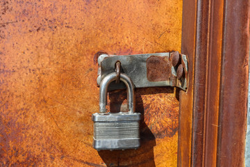 Open key lock hanging on closed orange rusty metal door - not very secure