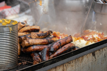 Pile of sausages and hotdogs on a hot grill that is smoking.