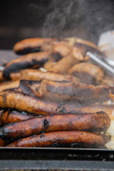 Pile of sausages and hotdogs on a hot grill that is smoking.