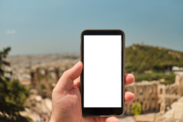 hand of man holding smart phone in front of the ancient area o the Athens Greece, theater under acropolis - Odeon of Herodes Atticus near Acropolis in a sunny day in the capital Greece - Athens.