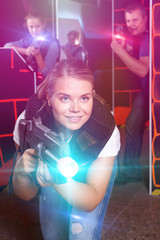 glad girl with laser pistol playing laser tag with friends