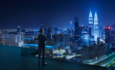 Businessman standing on open roof top balcony watching city night view . Business ambition and...