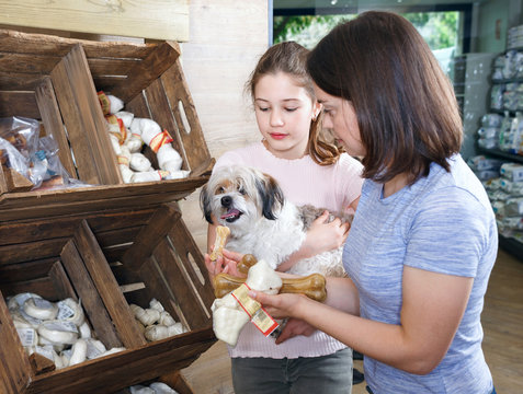 Mother With Teen Daughter Choosing Dog Treats For Their Puppy In Pet Supplies Store