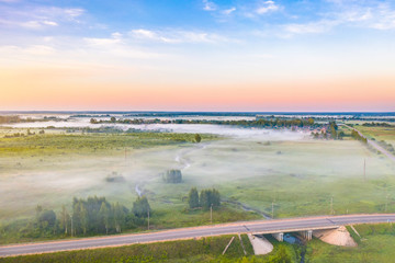 Aerial view of the morning fog road and bridge, among the meadows of fields and forests early in the morning.