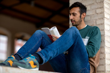 Young Bearded Man Reading A Book Sitting In A Park During The Morning