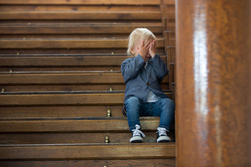 Sad child, sitting on a staircase in a big house, concept for bullying, depression