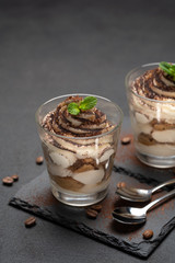 Classic tiramisu dessert in a glass on stone serving board on dark concrete background