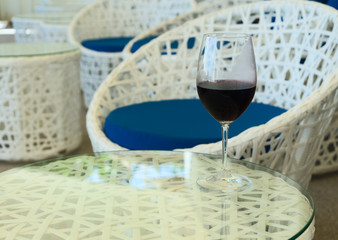 a glass of chilled red wine on a wicker table with a glass surface, closeup