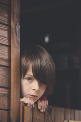 Fototapeta na wymiar Preteen boy in red sweatshirt, hiding behind a wooden door, looking scared