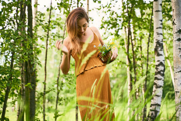 A young woman mother straightens her loose green dress standing among the green meadows and birches. The concept of pregnancy, ecology, natural beauty and unity with nature