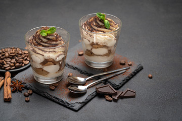 Classic tiramisu dessert in a glass on stone serving board on dark concrete background