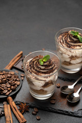 Classic tiramisu dessert in a glass on stone serving board on dark concrete background