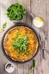 Quiche with arugula, onion, spinach, mozzarella, feta and sauce on rustic background, top view. Homemade, traditional french quiche pie.